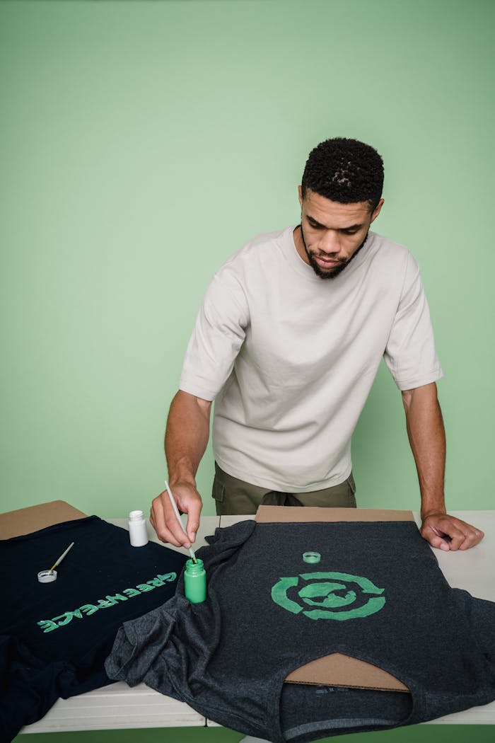 Home Man with beard painting custom designs on t-shirts in a studio setting.